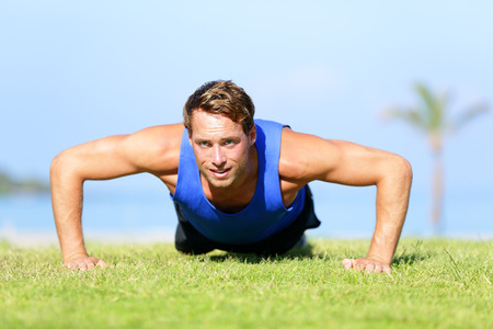 Push-ups - fitness man training push up outside in grass in summer. Fit male athlete working out...