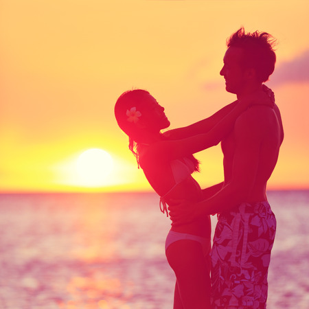 Romantic couple embracing kissing on beach at sunset. Two young lovers playful and happy together on honeymoon travel holiday vacation in summer on tropical beach. Happiness concept with man and womanの写真素材