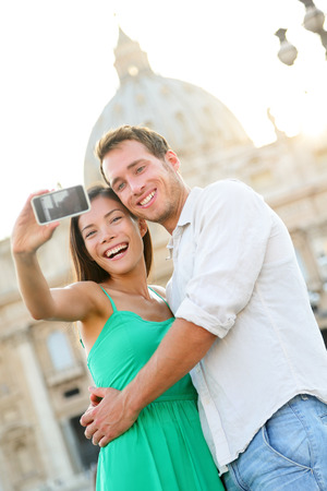 Tourists couple selfie by Vatican city and St. Peter's Basilica church in Rome. Happy travel woman and man taking selfie photo picture on romantic honeymoon in Italy.の写真素材