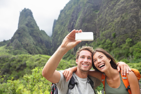 Couple taking selfie photo with smart phone hiking on Hawaii. Woman and man hiker taking photo with smart phone camera. Healthy lifestyle from Iao Valley State Park, Wailuku, Maui, Hawaii, USA.の写真素材