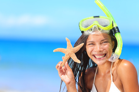 Beach travel people - woman with snorkel and starfish in bikini enjoying summer vacation holidays on tropical resort by ocean sea. Beautiful young mixed race Asian Caucasian woman smiling happy.の写真素材