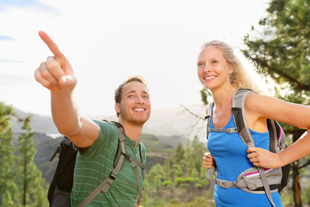 People hiking - couple on hike in forest. Hikers talking and pointing enjoying trek in beautiful mountain forest landscape. の写真素材