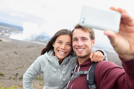Hawaii - couple sefile by Hawaiian volcano. Travel tourists happy taking self-portrait with smart phone by Halemaumau crater within the Kilauea Volcano caldera inside hawaii volcanoes national parkの写真素材