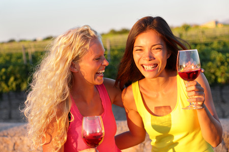 Happy women friends drinking red wine laughing in vineyard in summer.の写真素材