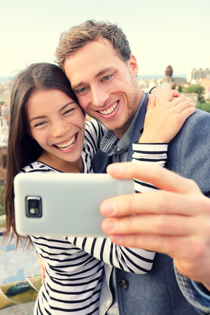 Selfie smartphone self-portrait by happy couple. Lifestyle photo with young friends or lovers taking picture with smart phone. Multiracial Asian woman and Caucasian man.の写真素材
