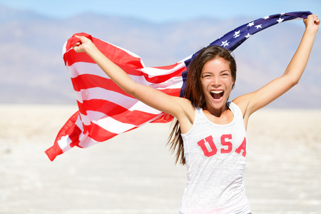 American flag - woman USA sport athlete winner cheering waving US flag Stars and Stripes outdoor running in nature. Beautiful cheering happy young multicultural girl joyful and excited.の写真素材