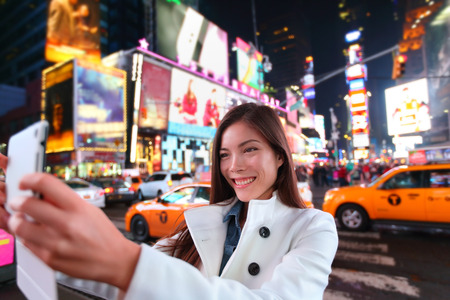 Happy woman tourist taking photo picture with tablet in New York City, Manhattan, Times Square. Girl traveler taking selfie joyful and happy smiling. Multiethnic Asian Caucasian woman in her 20s.の写真素材