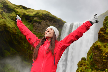 Happy woman by waterfall Skogafoss on Iceland posing serene and free outdoors. Girl visiting famous tourist attractions and landmarks in Icelandic nature landscape on Golden Circle.の写真素材