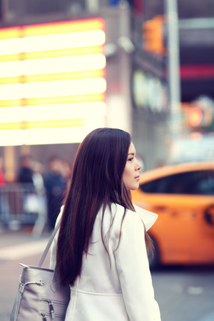 Woman in New York City Manhattan. Young urban professional business woman walking in street wearing coat downtown with yellow taxi cabs in background. Multiracial Asian Caucasian businesswoman in USA.の写真素材