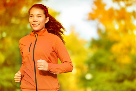 Runner woman running in fall autumn forest. Female fitness girl jogging on path in amazing fall foliage landscape nature outside.の写真素材
