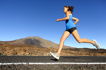 Sprinting running woman - female runner training outdoors jogging on mountain road in amazing...