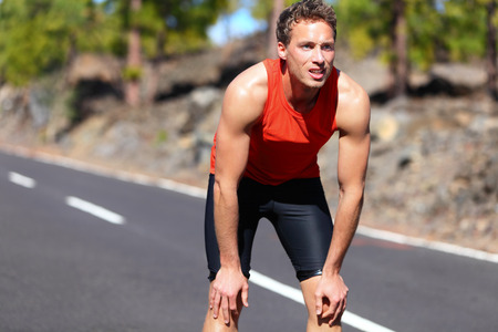 Runner resting after running. Jogging man taking a break during training outdoors in on mountain road. Young Caucasian male fitness model after work out.の写真素材