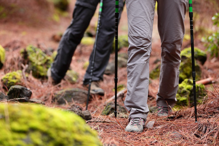 Hiking - Hikers walking in forest with hiking sticks on path trail in mountains. Close up of hiking shoes and boots. Man and woman hiking together.の写真素材