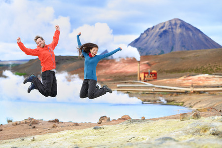 Iceland travel people jumping of joy in front of hot spring and geothermal energy power plant in NÃ¡mafjall in Lake Myvatn area. Happy couple on travel in Icelandic nature landscape, Route 1 Ring Road.の写真素材