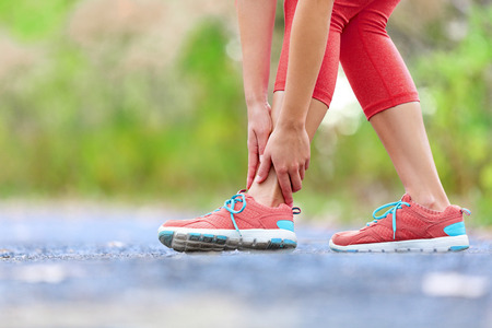 Twisted broken ankle - running sport injury. Female runner touching foot in pain due to sprained...
