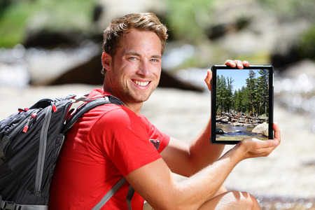 Hiking man showing nature forest picture on tablet. Young adult taking pictures with digital tablet computer of landscape in Yosemite National Park, California, USA.の写真素材