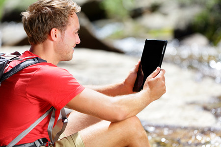 Tablet computer man hiker hiking in Yosemite, USA using travel app or map during hike, resting by river. Caucasian male hiker relaxing on a summer day.の写真素材