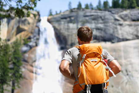 Hiker hiking with backpack looking at waterfall in Yosemite park in beautiful summer nature landscape. Portrait of male adult back standing outdoor.の写真素材