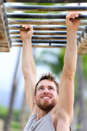 Fit man cross training on monkey bars station. Fitness workout on brachiation ladder in an outdoor gym outside. Male athlete swinging on high bars exercising.の写真素材