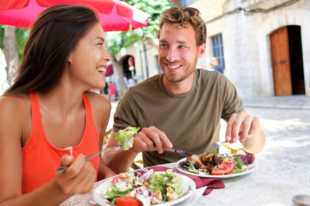 Restaurant tourists couple eating at outdoor cafe. Summer travel people eating healthy food together at lunch during holidays in Mallorca, Spain. Asian Caucasian multiracial young adults.の写真素材