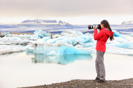 Nature landscape photographer taking picture photos with SLR camera on Iceland Jokulsarlon glacial lagoon / glacier lake. Woman taking photograph of beautiful Icelandic nature with Vatnajokull.の写真素材