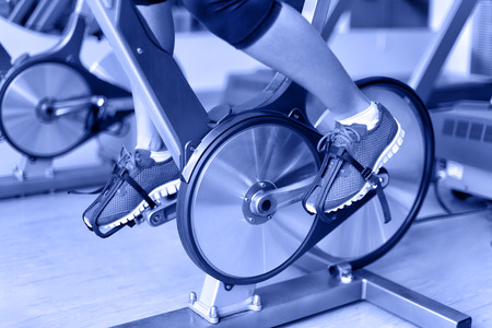 Exercise bike with spinning wheels. Woman excising biking in fitness center. closeup of pedals. Professional fitness center equipment.の写真素材