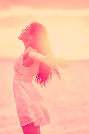 Freedom - Free happy serene woman enjoying sunset. Beautiful woman in dress embracing the golden sunshine glow of sunset with arms outspread and face raised in sky enjoying peace, serenity in natureの写真素材