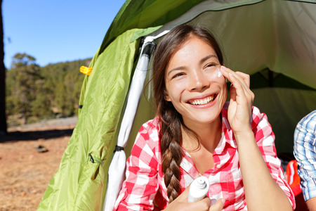 Camping woman applying sunscreen sun cream sunblock suntan lotion in tent smiling happy outdoors in forest. Happy biracial Asian Caucasian girl living healthy active lifestyle.の写真素材