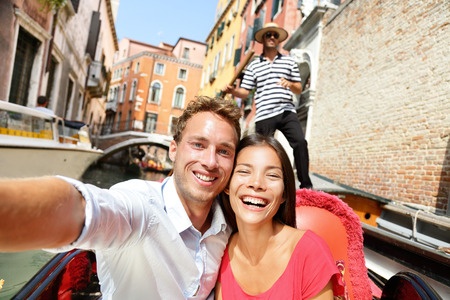 Selfie couple taking picture in gondola on Venice travel vacation. Beautiful lovers on a romantic boat ride across the Venetian canals taking self-portrait pictures with smartphone during holiday.の写真素材