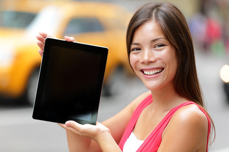 Tablet computer casual woman showing blank empty screen of tablet pc in New York City, standing in street with yellow taxi cab. Beautiful young mixed race female model in Manhattan, New York City.の写真素材
