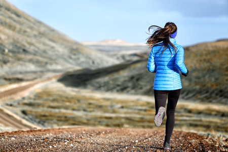 Woman winter and autumn running in down jacket. Female running jogging on mountain trail in beautiful landscape.の写真素材