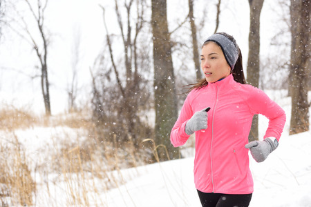 Winter jogging - young Asian Chinese adult woman runner running breathing cold air wearing pink jacket, headband and gloves doing a cardio workout.の写真素材