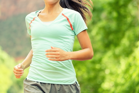 Running Woman Jogging. Midsection of determined woman runneron sunny day. Young female is in sports clothing. Sporty athlete runner is exercising against trees.の写真素材