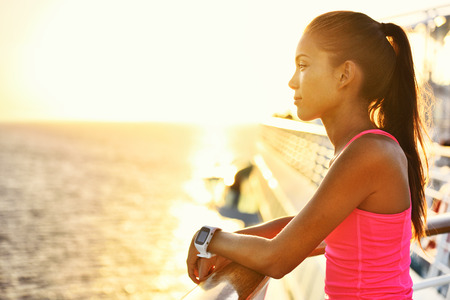 Active woman relaxing after run on cruise ship looking at the sea during summer holidays. Asian runner girl wearing smartwatch heart rate activity monitor living a healthy lifestyle.の写真素材