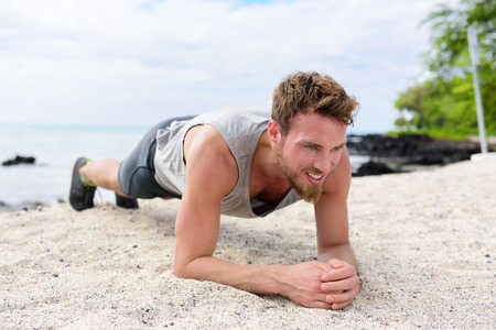Crossfit training fitness man doing plank core exercise working out his midsection muscles. Fit athlete fitness cross training planking exercising outside in sand on beach.の写真素材