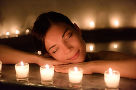 Beautiful young woman relaxing in hot tub at spa. Attractive female tourist is surrounded with lit...