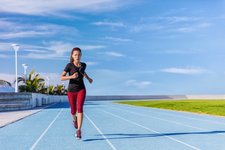 Female Asian athlete runner running on blue tracks at outdoor stadium in summer. Sporty woman...