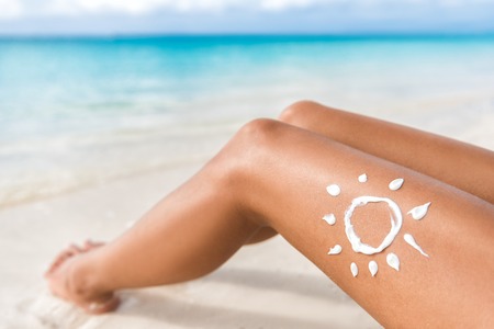 Sunscreen sun drawing lotion on suntan legs relaxing tanning on tropical beach holiday. Women lower...