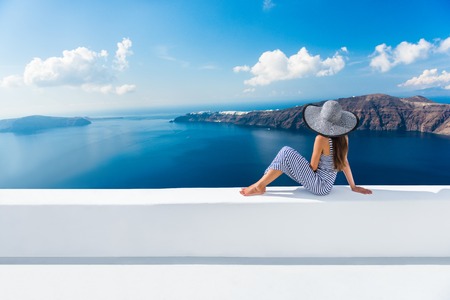 Europe Greece Santorini travel vacation. Woman looking at view on famous travel destination. Elegant young lady living fancy jetset lifestyle wearing dress on holidays. Amazing view of sea and Calderaの写真素材