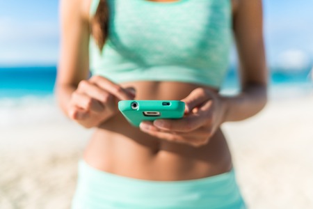 Athlete using mobile phone app fitness tracker for tracking weight loss progress during running exercise. Fit girl woman touching smartphone texting or playing online games or video workouts.の写真素材