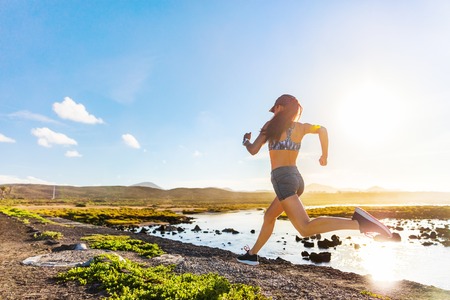 Athlete runner trail running on summer trail beach. Active morning jogging motivation woman sprinting with energy and motion in outdoors nature training cardio race in shorts and sports bra, shoes.の写真素材
