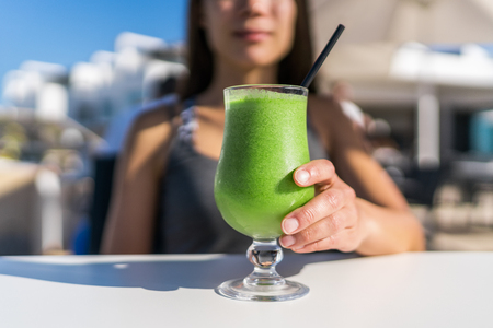 Healthy juicing lifestyle trend woman drinking green spinach juice smoothie cup at restaurant table. Unrecognizable person holding glass of fresh vegetables blend for a vegetarian diet detox cleanse .の写真素材