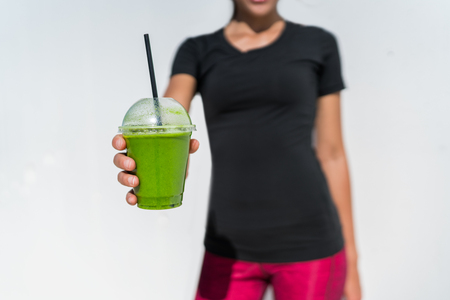 Healthy eating lifestyle fitness athlete woman drinking green smoothie cup for vegan weight loss diet. breakfast juicing trend. Person showing plastic container at outdoor cafe or juice bar.の写真素材