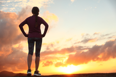 Active woman looking ahead at sunset sky for life challenge. Runner athlete getting ready for trail run thinking goal achievement choice and happiness. Female sports person living healthy lifestyle.の写真素材