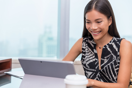 Asian woman smiling at laptop screen doing video chat conference online or working at office desk. Freelance work at home or customer service support.の写真素材