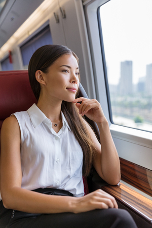Woman enjoying view in train commute. Woman relaxing enjoying view during morning commute. Business class seat in train. Asian businesswoman pensive looking out the window in travel transport.の写真素材