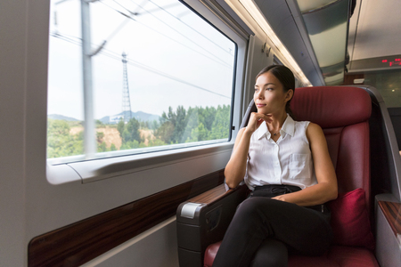 Woman relaxing enjoying view during morning commute. Business class seat in train. Asian businesswoman pensive looking out the window in travel transport.の写真素材