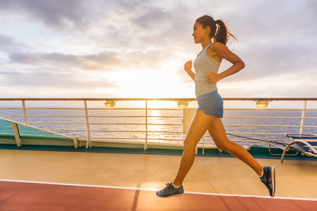 Cruise ship passenger doing morning jogging on deck running tracks with sunrise sunshine. Woman tourist enjoying fitness training during Caribbean travel vacation.の写真素材