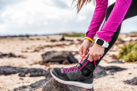 Fitness smartwatch woman runner lacing running shoes on beach, Athlete girl getting ready for run workout tying running shoe laces outside wearing watch gear. Healthy lifestyle concept.の写真素材