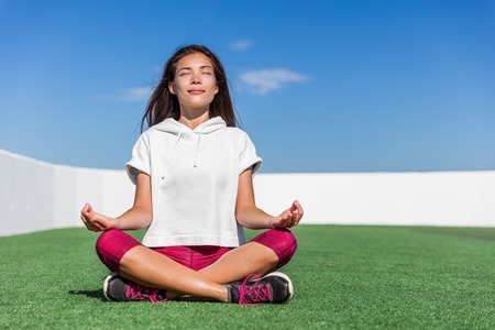 Yoga fitness woman doing summer meditation outdoor. Happy asian athlete meditating before strength training workout sitting in lotus position on outside grass gym floor. Active living.の写真素材